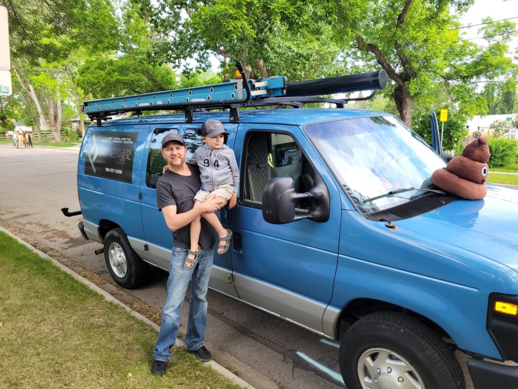 Coleton Fallis, the owner of Flawless Flows LTD in Alberta Canada holds his young son while standing in front of his work truck
